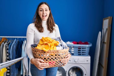 Young hispanic woman holding laundry basket celebrating crazy and amazed for success with open eyes screaming excited. 