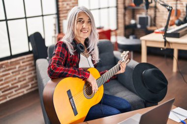 Müzik stüdyosunda klasik gitar çalan gri saçlı kadın müzisyen.