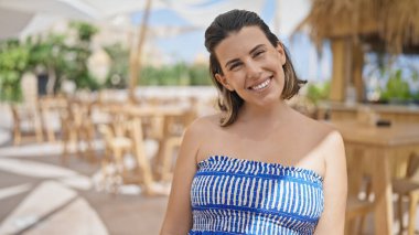 Genç İspanyol kadın mutlu bir şekilde gülümsüyor güneşli restoran terasında kameraya bakıyor.
