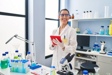 Genç ve güzel İspanyol bilim kadını. Laboratuvarda dokunmatik ped kullanarak gülümsüyor.