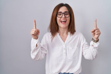 Esmer kadın izole edilmiş beyaz arka planda duruyordu. Şaşırmış, şaşırmış, parmaklarıyla işaret ediyor ve kollarını kaldırıyordu.. 