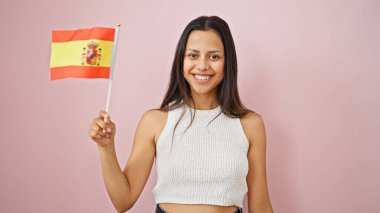Genç, güzel, İspanyol bir kadın gülümsüyor. İspanyol bayrağını soyutlanmış pembe arka planda tutuyor.