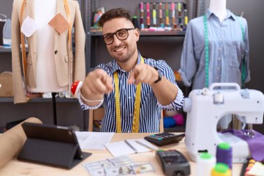 Atölyede çalışan İspanyol asıllı terzi seni ve kamerayı işaret ediyor, gülümsüyor, pozitif ve neşeli. 