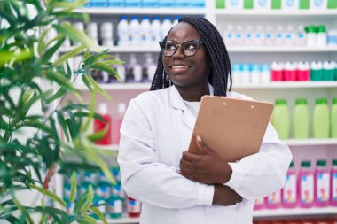 Afro-Amerikalı kadın eczacı gülümseyerek eczanede kendine güvenen bir pano tutuyor.