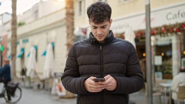 Kahve dükkanının terasında akıllı telefon kullanan genç bir İspanyol.