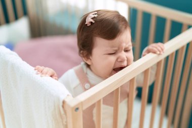 Adorable toddler standing on cradle crying at bedroom