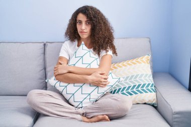 Evdeki kanepede oturan kıvırcık saçlı İspanyol kadın yüzünde ciddi bir ifadeyle rahatlamış. Basit ve doğal bir şekilde kameraya bakıyorsun.. 