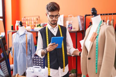 Genç İspanyol terzi dokunmatik ped kullanıyor. Atölyede duruyor.