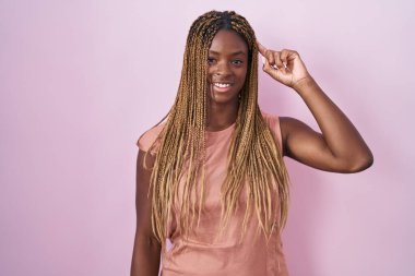 Pembe arka planda örülü saçları olan Afrikalı Amerikalı bir kadın. Tek parmakla gülümseyerek, harika bir fikir ya da düşünceyle, iyi bir hafızayla. 