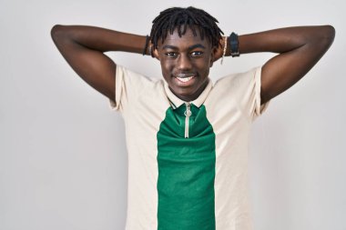 Afrikalı bir adam izole edilmiş arka planda duruyor, rahatlıyor ve esniyor, kolları ve elleri başının ve boynunun arkasında mutlu bir şekilde gülümsüyor. 