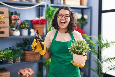 Young hispanic woman working at florist shop smiling and laughing hard out loud because funny crazy joke. 