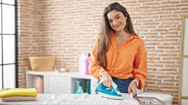 Genç ve güzel İspanyol kadın gülümsüyor çamaşırhanede kendine güvenen ütü yapıyor.