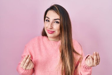 Pembe arka planda duran genç İspanyol kadın elleriyle para hareketi yapıyor, maaş istiyor, milyonerlik işi yapıyor. 