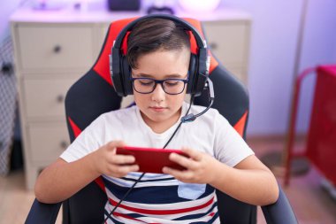 Oyun odasında akıllı telefon kullanarak video oyunu oynayan tapılası İspanyol asıllı çocuk.