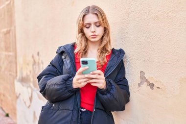 Sokakta akıllı telefon kullanan genç sarışın kadın.
