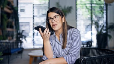 Genç, güzel, İspanyol bir kadın ofisteki sandalyede oturan telefonla sesli mesaj yolluyor.