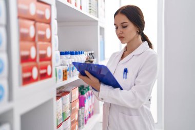 Young woman pharmacist writing on clipboard at pharmacy