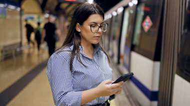 Madrid metro istasyonunda akıllı telefon kullanan güzel İspanyol bir kadın metroda bekliyor.