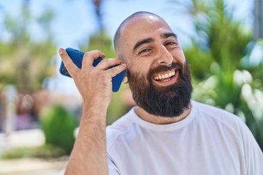 Genç kel adam gülüyor. Parktaki akıllı telefondan kendine güvenen sesli mesaj dinliyor.