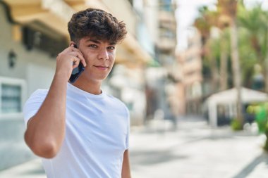 Latin kökenli genç, gülümsüyor ve caddede akıllı telefondan konuşuyor.