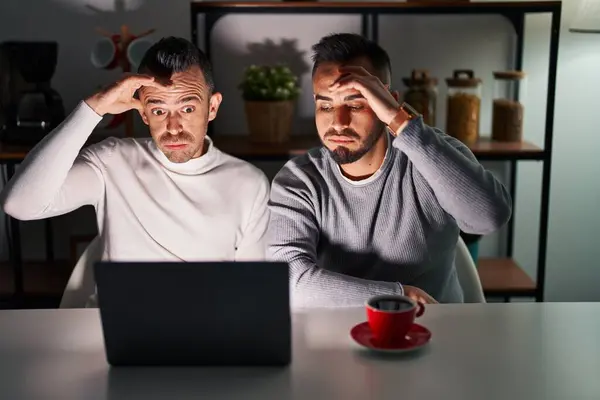 Homosexual couple using computer laptop worried and stressed about a problem with hand on forehead, nervous and anxious for crisis