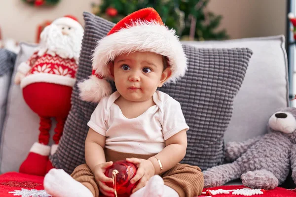 Αξιολάτρευτο Ισπανόφωνο Μωρό Κρατώντας Χριστουγεννιάτικη Διακόσμηση Μπάλα Κάθεται Στον Καναπέ — Φωτογραφία Αρχείου