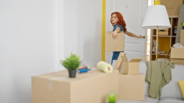 Young redhead woman coming home holding package at new home
