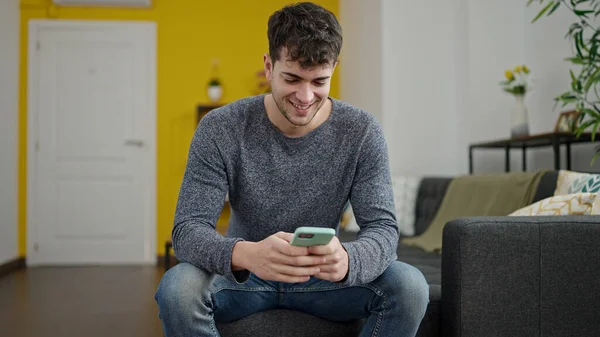 Evdeki Kanepede Oturmuş Gülümseyen Akıllı Telefon Kullanan Spanyol Genç Adam — Stok fotoğraf