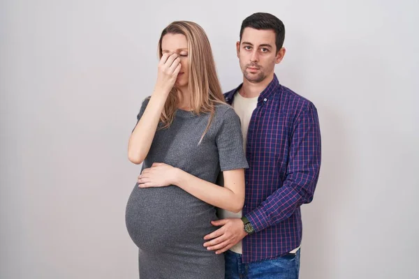 白い背景の上に立っている赤ん坊を期待する若いカップル疲労と疲労と頭痛を感じる鼻と目 ストレスとフラストレーションの概念 — ストック写真