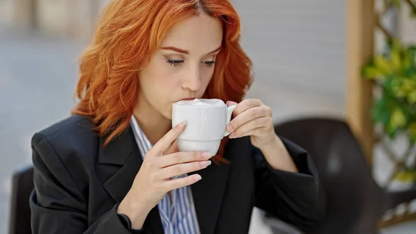 Young redhead woman business worker drinking cup of coffee at coffee shop terrace