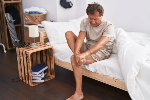 Middle age man suffering for feet pain sitting on bed at bedroom