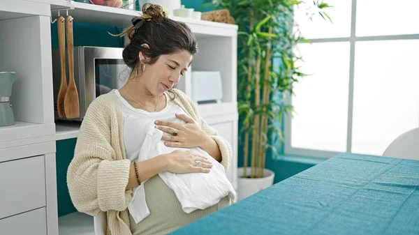 Νεαρή Έγκυος Γυναίκα Που Κρατά Μωρουδιακά Ρούχα Κάθεται Στο Τραπέζι — Φωτογραφία Αρχείου