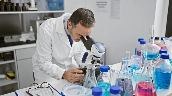 一个白发苍苍的老人 一个忙于实验室工作的科学家 凝视着显微镜寻找医学发现 — 图库照片