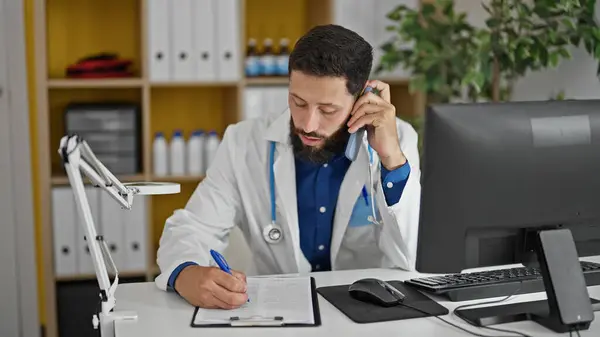 Jovem Hispânico Homem Médico Falando Smartphone Escrevendo Relatório Médico Clínica — Fotografia de Stock