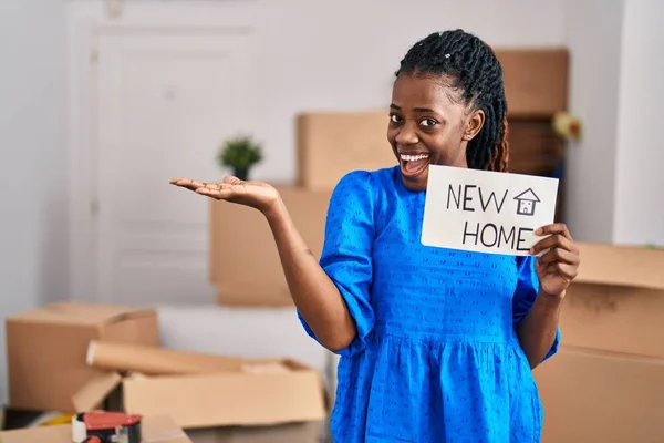 African woman with braided hair moving to a new home holding banner celebrating achievement with happy smile and winner expression with raised hand