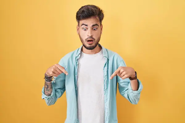 Sarı Arka Planda Dikilen Dövmeli Genç Spanyol Adam Parmaklarını Göstererek — Stok fotoğraf
