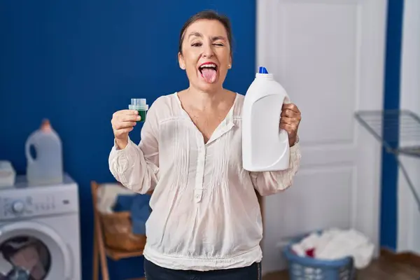 Middle Age Hispanic Woman Holding Detergent Bottle Sticking Tongue Out — Stock Photo, Image