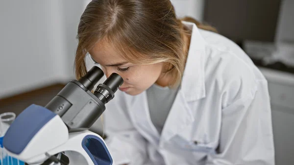 In the heart of science, young attractive blonde woman scientist intently working with microscope at laboratory, brewing discoveries through analysis