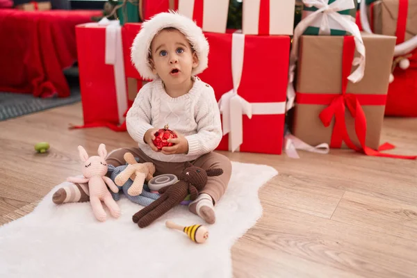 家の床に座っているクリスマスボールの装飾を保持する好ましいヒスパニックの幼児 — ストック写真