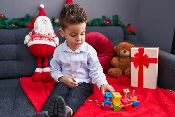 自宅でクリスマスの装飾でソファーに座っている列車のおもちゃで遊ぶ愛らしいヒスパニックの幼児 — ストック写真