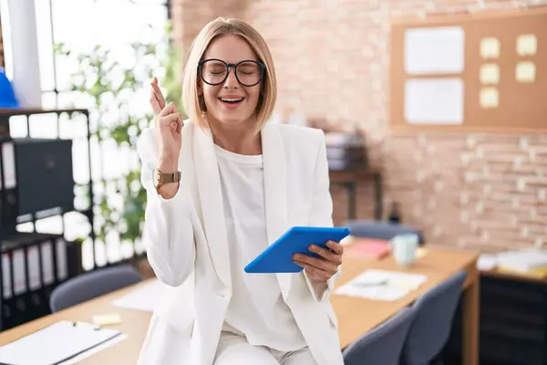 stock image Young caucasian woman working at the office wearing glasses gesturing finger crossed smiling with hope and eyes closed. luck and superstitious concept. 