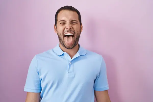 ピンクの背景の上に立っているヒスパニックな男性は 面白い表現で幸せな舌を出します 感情コンセプト — ストック写真