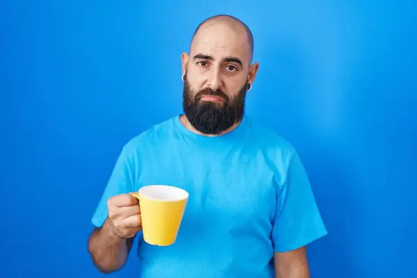 Young hispanic man with beard and tattoos drinking a cup of coffee depressed and worry for distress, crying angry and afraid. sad expression.