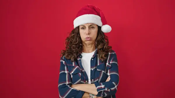 Латиноамериканка Средних Лет Стоящая Расстроенная Рождественской Шляпе Изолированном Красном Фоне — стоковое фото