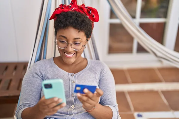 アフリカ系アメリカ人女性ラップトップとクレジットカードを使用してホームテラスでハンモックに横たわって — ストック写真