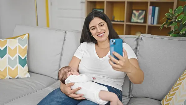 自宅でセルフィー写真を撮るソファに座っている母と赤ちゃんの娘 — ストック写真