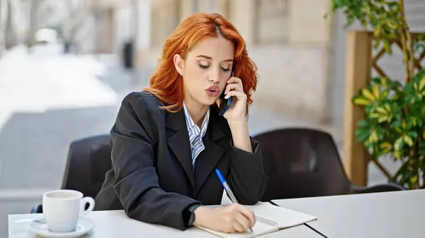 年轻的红头发女商人在咖啡店的露台上用智能手机记笔记 — 图库照片