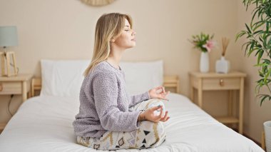 Genç sarışın kadın yoga egzersizi yapıyor. Yatak odasında oturuyor.