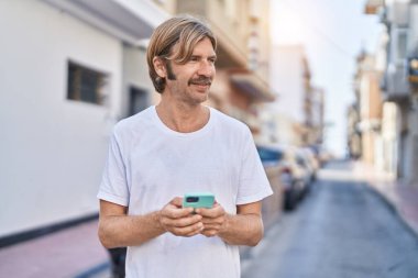 Young blond man smiling confident using smartphone at park