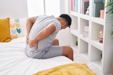 Sırtından yaralanan Çinli genç bir adam yatak odasında oturuyor.